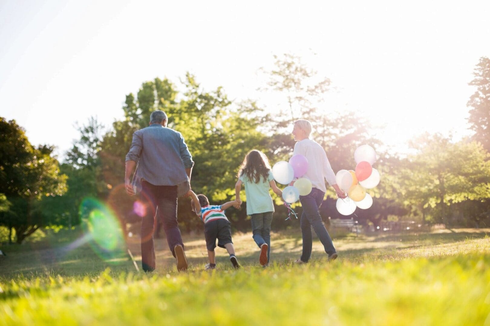 A family walking in the grass with balloons.